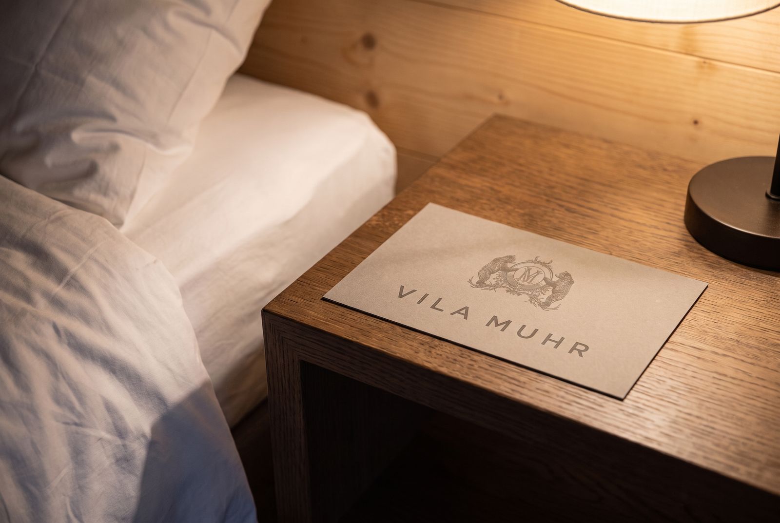 Guest card with the Vila Muhr wordmark on a bedside table